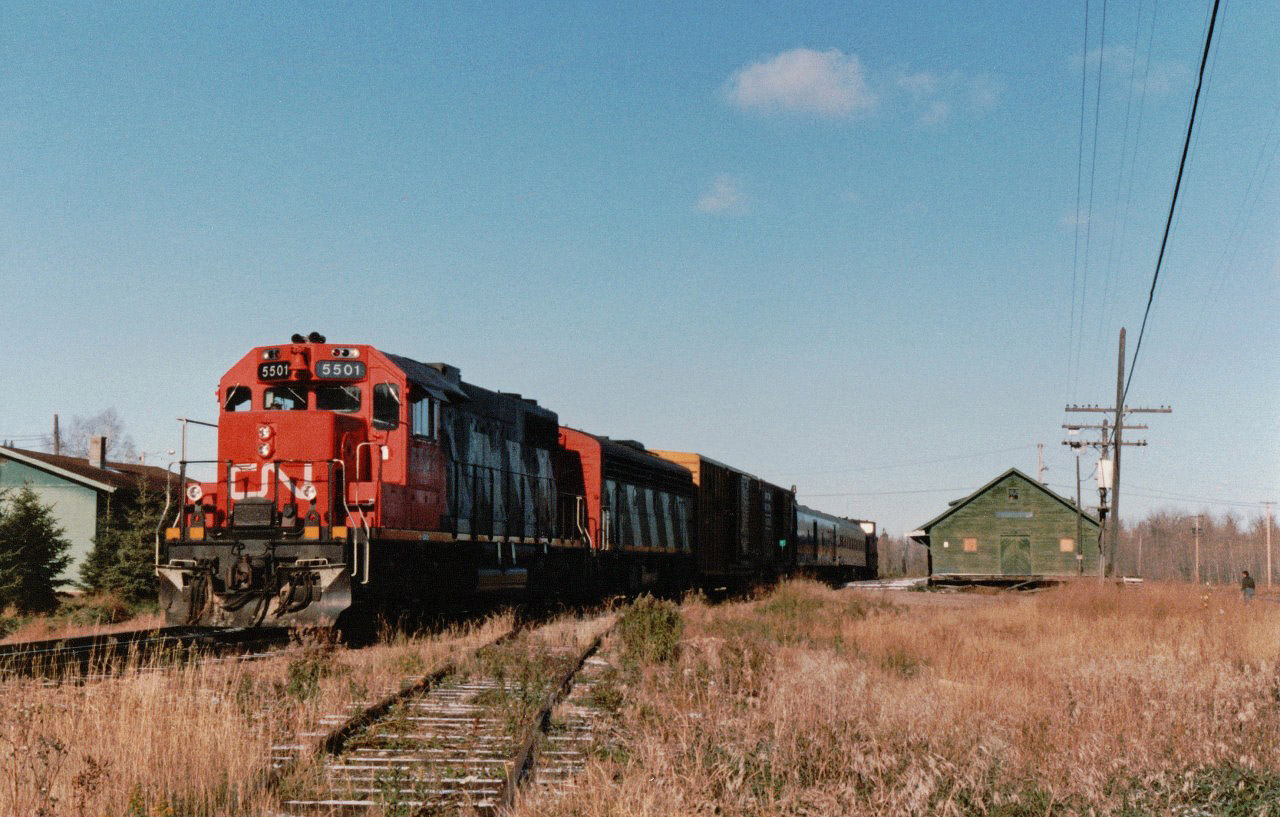 On a Friday morning in October 1987, CN 5501 is ready to leave Waterways, Alberta, the  station for Fort McMurray, a short distance to the north and long before that community became associated in the minds of most of us with oil sands.  Train 289, the northbound counterpart of train 290, known locally as the “Muskeg Mixed”, took two days, with a overnight stopover in Lac La Biche, for the 294 mile journey which explains why our group of three chose a Red Arrow bus for the northbound leg and the CN mixed train for the southbound trip scheduled to take just under 11 hours.  Coupled immediately ahead of the caboose is coach 5099, built for CN in 1937 as 5209, transferred to VIA Rail in 1978, and reacquired and renumbered in 1982 by CN which fitted it with a diesel generator to provide power for lighting and cooling.  Imagine, an air-conditioned coach on a lowly mixed train!.  In another respect the train was unusual because it was at the time the only passenger train still operated by CN in its own name, all others having been discontinued or turned over to VIA Rail.  After several false starts going back as far as 1909, the line had been completed in 1925 by the Alberta & Great Waterways Railway and subsequently became a part of the Northern Alberta Railways. . 

The schedule, which called for departure at 11:00 and arrival at 21:45, was adhered to somewhat casually for most of the southward trip which saw a few passengers embark and disembark along the way.  There was little switching in or out of  freight cars.  As we neared Edmonton, now with only our group of three intrepid riders remaining, progress became very much stop-and-go.  The conductor’s repeated calls to the dispatcher asking for permission to enter North Edmonton yard because he had passengers on board made us realize that, quite possibly, we were a rarity and that few actually rode the entire length of the line.  Finally, some time after midnight, about three hours late, we were able to leave the train.   A patient friend, who had offered to drive us to Calgary that night was still waiting for us.
