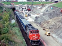 Canadian National's St. Clair Tunnel at Sarnia was too small to handle higher cars such as double stacks, so the decision was made to bore a new, larger tunnel. A special ceremony was held on September 16th 1993 to celebrate the start of the new bore. The old tunnel was built in 1891, 6025 feet long and had a bore diameter 19 feet 10 inches. The new tunnel would be opened in 1994, 6129 feet long and have a bore diameter of 27 feet 6 inches.
<br><br>
Here is a special passenger train that took special guests through the old tunnel to Port Huron, where there was an elaborate lunch before the return trip. There was also a ceremonial function in a large tent in Sarnia.
<br><br>
In the photo we see the passenger special, made up of two CN GP40-2W's bracketing 5 VIA passenger cars, starting through the old tunnel on the left. The green paint showing on the bell of CN 9674 gives off her former GO Transit heritage (one of 10 purchased from GO a few years back). On the right the Lovat TBM (tunnel boring machine) is ready to start the new bore.