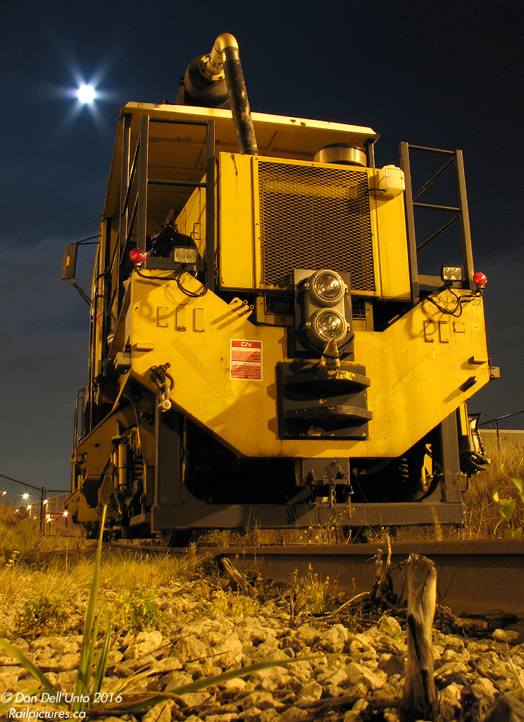 Under a Full Moon at Bramalea: CN Plasser Dynamic Track Stabilizer (PTS-90) 619-32 sits on the long-disused but recently trimmed siding to logistics distributor Kuehne + Nagel's Bramalea warehouse, near the namesake GO station. It is but one piece of track equipment in the area working on the then-ongoing triple tracking of the Halton Sub through Brampton.  The little piggy strapped in front of the Pyle National dual sealed beam headlight was no doubt the work of one of the track gang members...
