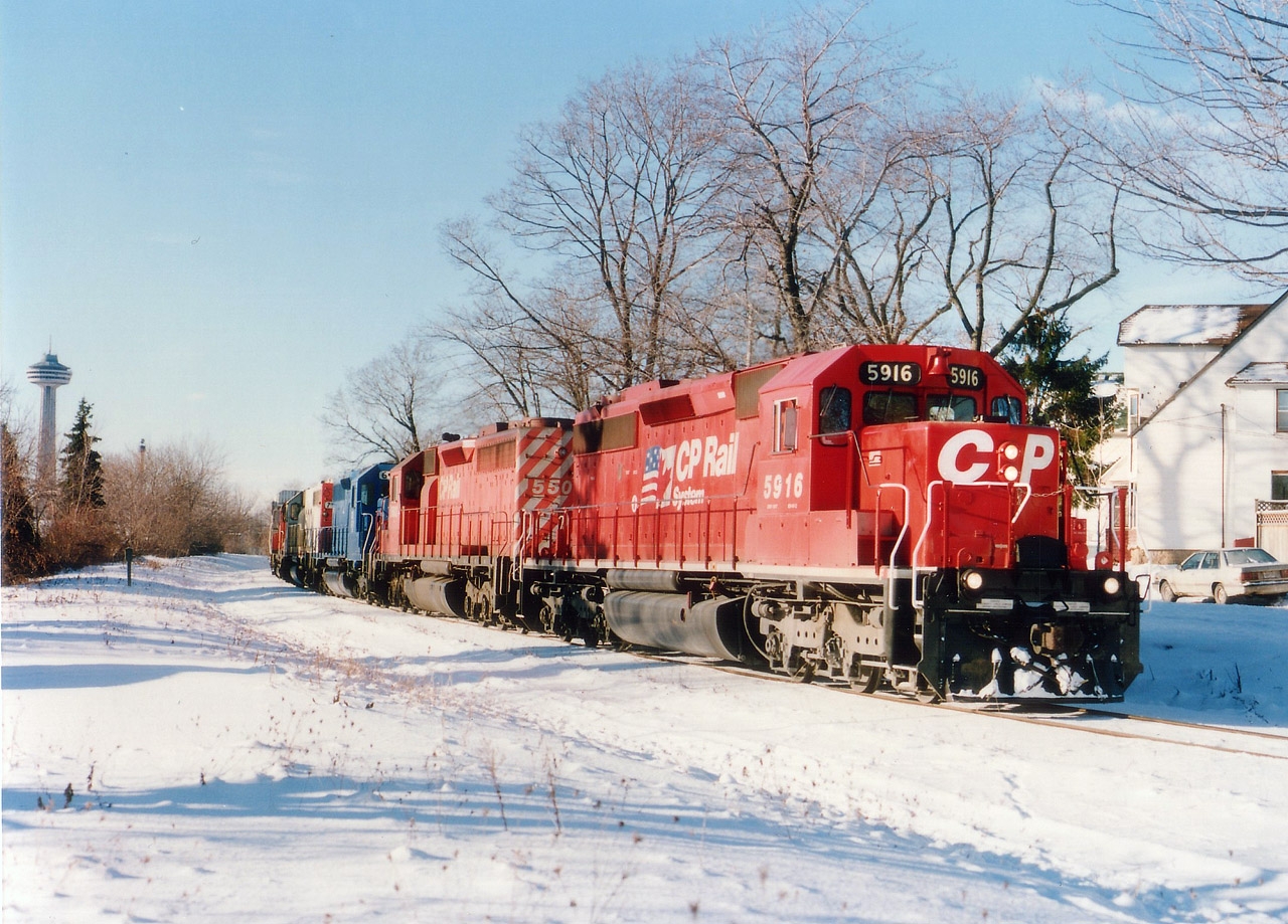By Mile 1, meaning one mile from the bridge over the Niagara River and the USA, CP 5916, 5502, CRL 611, SOO 760 and CP 4214 are seen having just passed thru the commercial/tourist district of Clifton Hill. Palmer Av is the street which parallels the tracks. The old trackbed is now a walking trail.