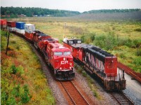 Shared assets in the Shared Asset Zone.  CP #102 with 8705 and 9113 snakes southward past CN 5257 & Van 79707 waiting it out on the MoW siding. View long-lensed from Hwy 69 overpass. Medium format 120- 400 ISO film for anyone interested. From near Parry Sound to just south of Sudbury CN and CP share trackage. CN line is used for southbounds, CP track for northbounds.