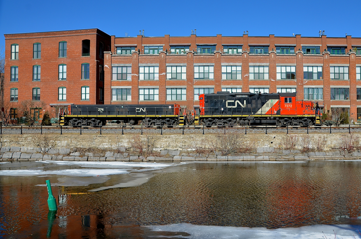 Passing the old Stelco mill. GP9 CN 7272 & slug CN 274 are heading light along the East Side Canal Bank Spur on their way to Robin Hood mill to pick up 7 empties. They are passing what was part of the Stelco steel mill, now it is part of a condo complex. Once a common sight along both sides of the Lachine Canal, trains are now very rare, with Robin Hood mill being the only rail-served client along the length of the entire canal.