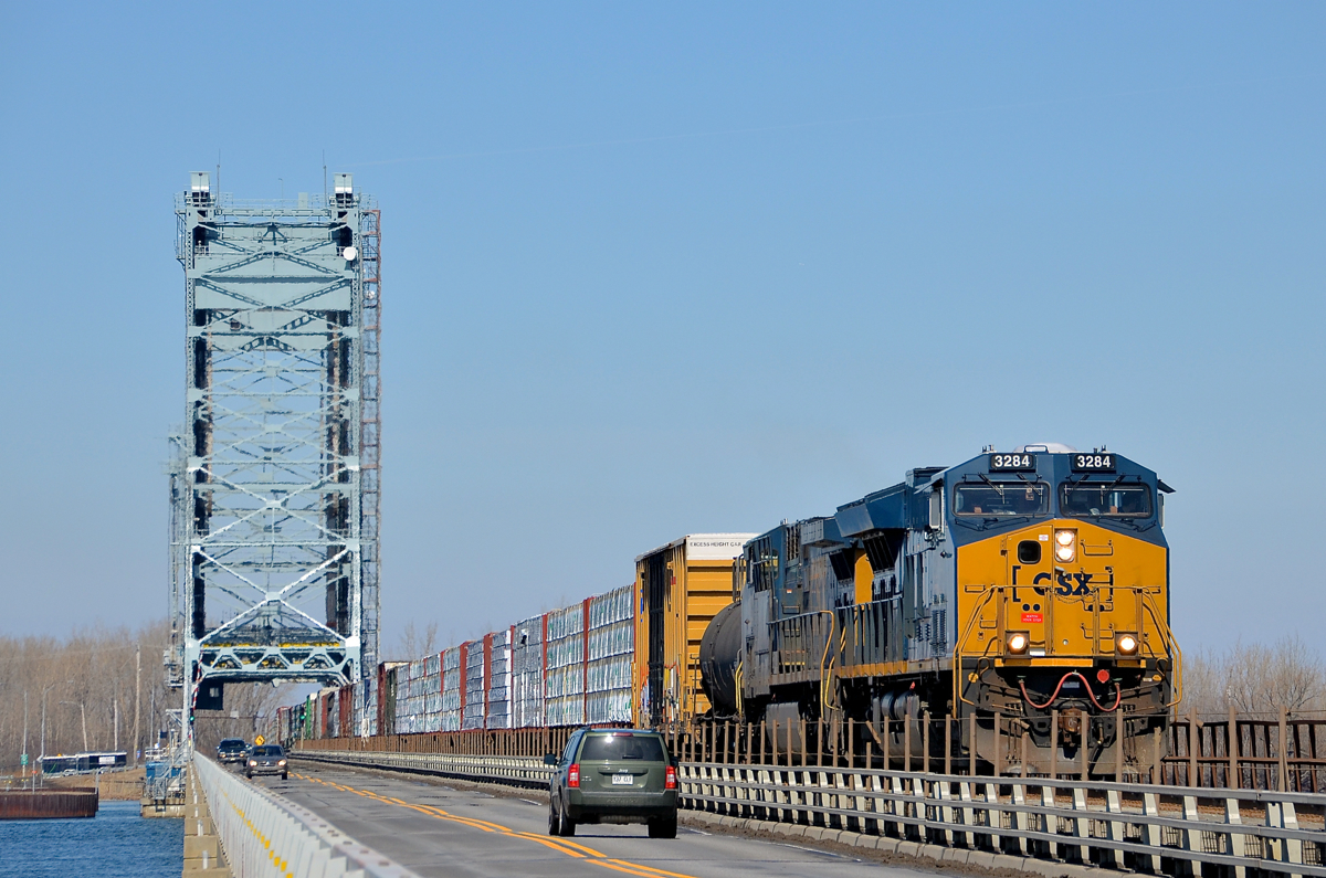Sharing the bridge with road traffic. The Saint-Louis-de-Gonzague bridge over the Beauharnois canal has 2 lanes for road traffic, as well as a single track for CSXT's Montreal sub. Here CN 327 is crossing over the bridge with new unit CSXT 3284 leading. Trailing is CSXT 5101.