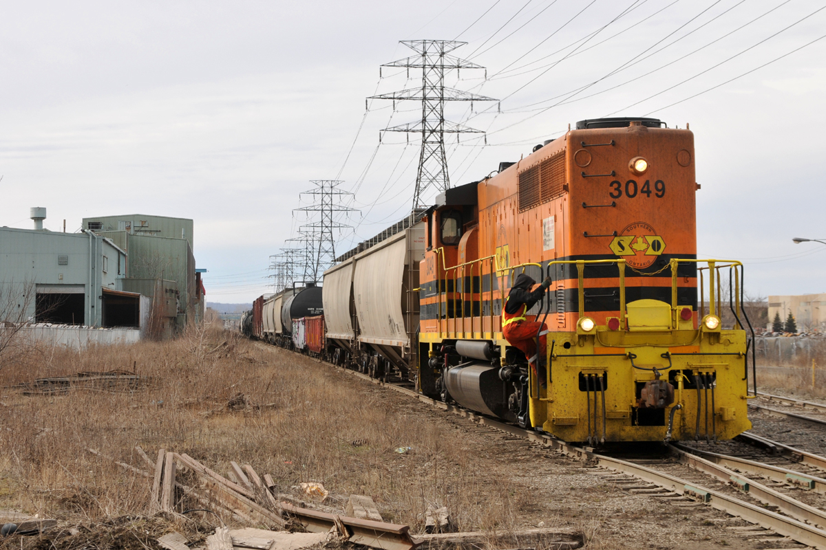 RLHH 3049 approaching Ottawa Street with 20 or so cars, as the conductor prepares to dismount to flag the crossing