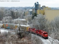 Winter has briefly returned, with an overnight ice storm  the trees are  white and drooping with the added weight. <br><br> What's in this scene? Top right is the rather tall Dover flour mill (Now owned by P&H) continuing to churn out product, and a former Rail customer (the siding went between the left of the mill and the office at left) -  that office is the former Grand River Railway head office building, now preserved and used by an advertising agency. I would imagine many 'fans who wanted to get permission to shoot the Preston Shops (which were to left out of sight) and all the GRR power and motors would have had to go into this building to get permission. (Anyone remember for sure?) <br><br>Back to the train -  T72 has 51 cars in tow and the motive power  growls  as the crew accelerates the RPM for the 2.5% grade.  I have done this scene before, <a href=http://www.railpictures.ca/?attachment_id=9694 target=_blank> back in 2007..</a>  and one can see it's growing in and getting difficult to pull off!