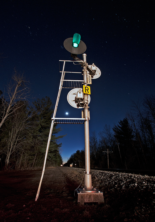 The headlights of a westbound  light up the RoW as this old US&S signal display a clear signal for the train crew on this somewhat mild evening.