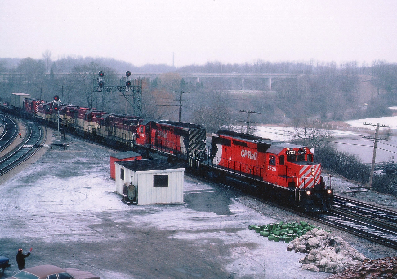 Its a crappy looking day, so out I go. There is always something of interest along the RR on a crappy day. And it is a Sunday. The TH&B "starlite" to me often was earlier on a weekend, and this day it rolled by around the dinner hour. Nice lashup. As you can see, cold and damp; lots of plates and spikes piled up for some maintenance work I have forgotten about..I don't like this sort of clutter in the shot, but looking back; hey, its all railroad related. Engineer waving to a trainwatcher whose name escapes me. Power on this version of the popular train is CP 5725, 5722, TH&B 401, 402, 403, 55 and CP 8791.