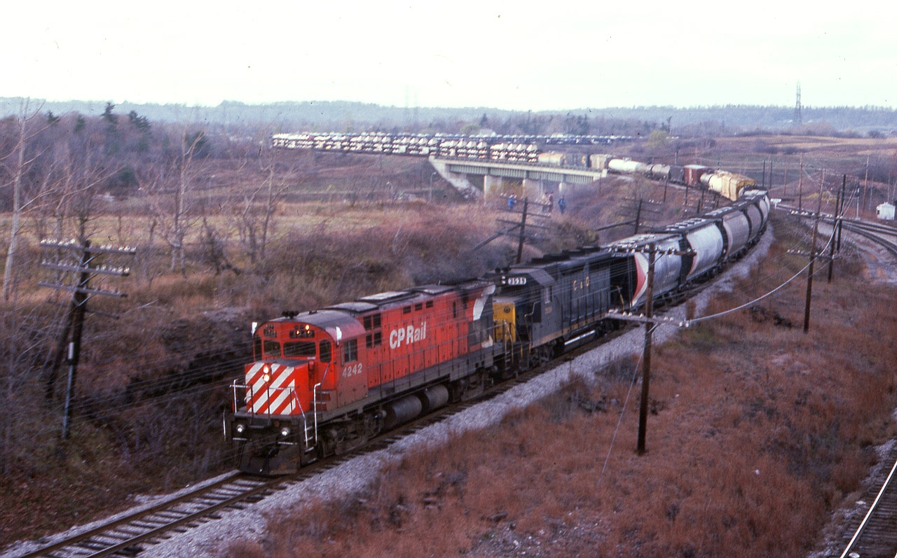 A long time back, (image 12431) I posted the first Detour Train that I witnessed courtesy of the infamous Mississauga Wreck of Nov. 1979. This incident was caused by a night-time derailment in Mississauga of CP train #54, a burned off wheel mid-train caused a pile-up and explosion that resulted in the evacuation of more than 200,000 people. A few following trains caught in the resulting closure of the line detoured down from Guelph Jct into Hamilton and then eastward to Toronto. This was the second train I caught, and it is rather late in the afternoon already. CP 4242 and C&O 3539 snake down over the Hwy 403 bridge with what is a rather amazing number of autos and truck cabs on the old style wide open carriers. Prone to vandals! By this time of the day word has gotten out and rather than just the one lone fan on the hillside overlooking the highway, we see 4 or 5 in this image.