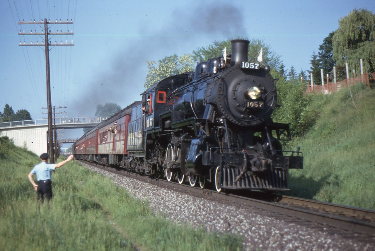 PC Ron Parker gives a wave to Engineman Frank Bunker as the 1057 has just passed under Elgin Street, Bowmanville on June 22/74. At this time 1057 belonged to the Ontario Rail Foundation and was leased to the Bytown Railway Society in Ottawa along with the coaches lettered 'Credit Valley'. The National Museum of Science and Technology organized and administered the Wakefield steam trips with Bytown Railway Society providing operating and maintenance assistance. They used 1057 for the summers of 1973 to 1975 while 1201 was being rebuilt. The ORF purchased 1057 from Herb Hanson of Chicago in 1972. The equipment moves from Toronto to Ottawa were one-way fan trips. Thanks to Bruce Chapman, John Mellow and Earl Roberts for some of these details.
