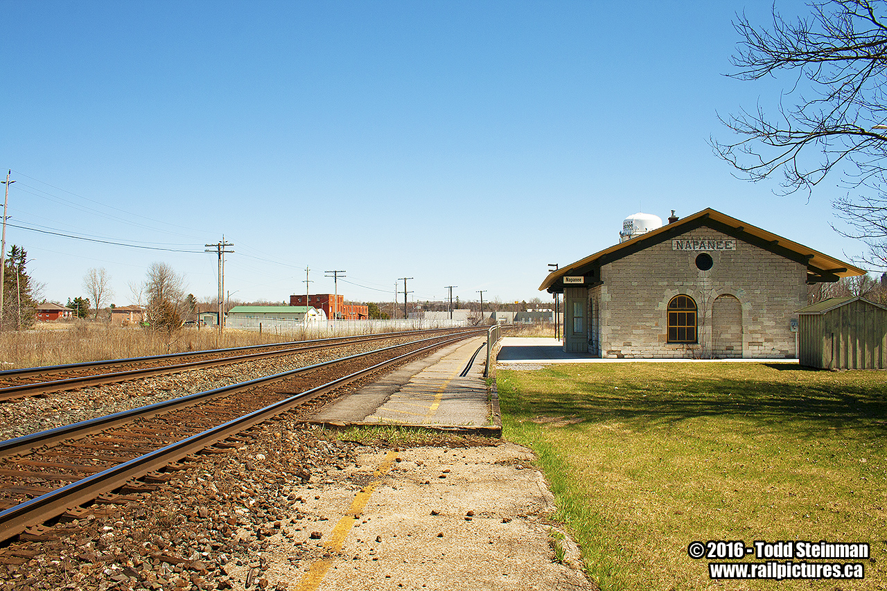 Napanee is another fine example of the architecture used when the Grand Trunk built it's many stone stations on the Toronto - Montreal mainline. I took a wide angled shot to show the surroundings, as it has changed in the many years from my first visit to the grounds as a youngster. 

Just to my left, is what used to be the Canadian Northern mainline that went to Smiths Falls. This line remained until the late 80's early 90's, where it was trimmed down to become a spur leading only to the Goodyear plant. Eventually, Goodyear closed and recently the spur removed. I was also saddened to come here on this trip and find all the fencing that had been installed recently...but then was reminded of a "Letter to the Editor" article I had written to both local papers almost 20 years ago. In that article, I had called out that fencing should be put up, after my own encounter with the Ontario Provincial Police.

Some of the original platform remains at each end of the station, which i can recount standing on in one of my many trips to this location. You can see how much the line has been built up, and I should also be happy  that the station remains too. Sometimes all you have is memories...and if I had stayed for only another 10 minutes I would have captured a westbound VIA on the curve speeding towards Belleville.