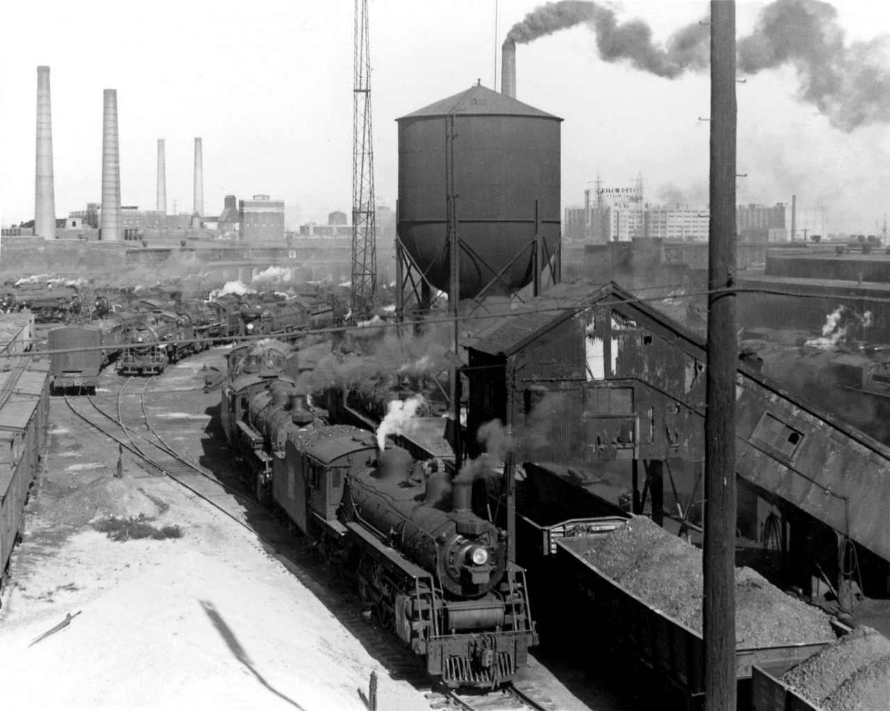 Not a diesel in sight! Steam still reigns supreme at Canadian National's Spadina roundhouse and shop facilities in 1952, as various sizes of steam engines from small switchers to big Northerns sit in downtown Toronto ready for their next assignments.

In the background, one can see various smokestacks (coal was the norm for heating) including those of the Central Heating Plant near CPR's neighbouring John St. Roundhouse. The White Rose gasoline signage in the background is on the roof of the Terminal Warehouse building, along the harbourfront.