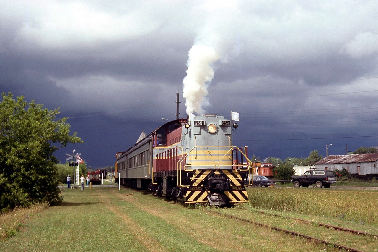 On August 1st 1991, the CRHA Annual Conference (in Kingston that year) traveled to Smiths Falls for a tour of the Railway Museum of Eastern Ontario. Former Canadian Pacific S3 6591 was operating on a short "excursion train" that day, and is shown running past the highway ahead of black storm clouds looming in the sky.