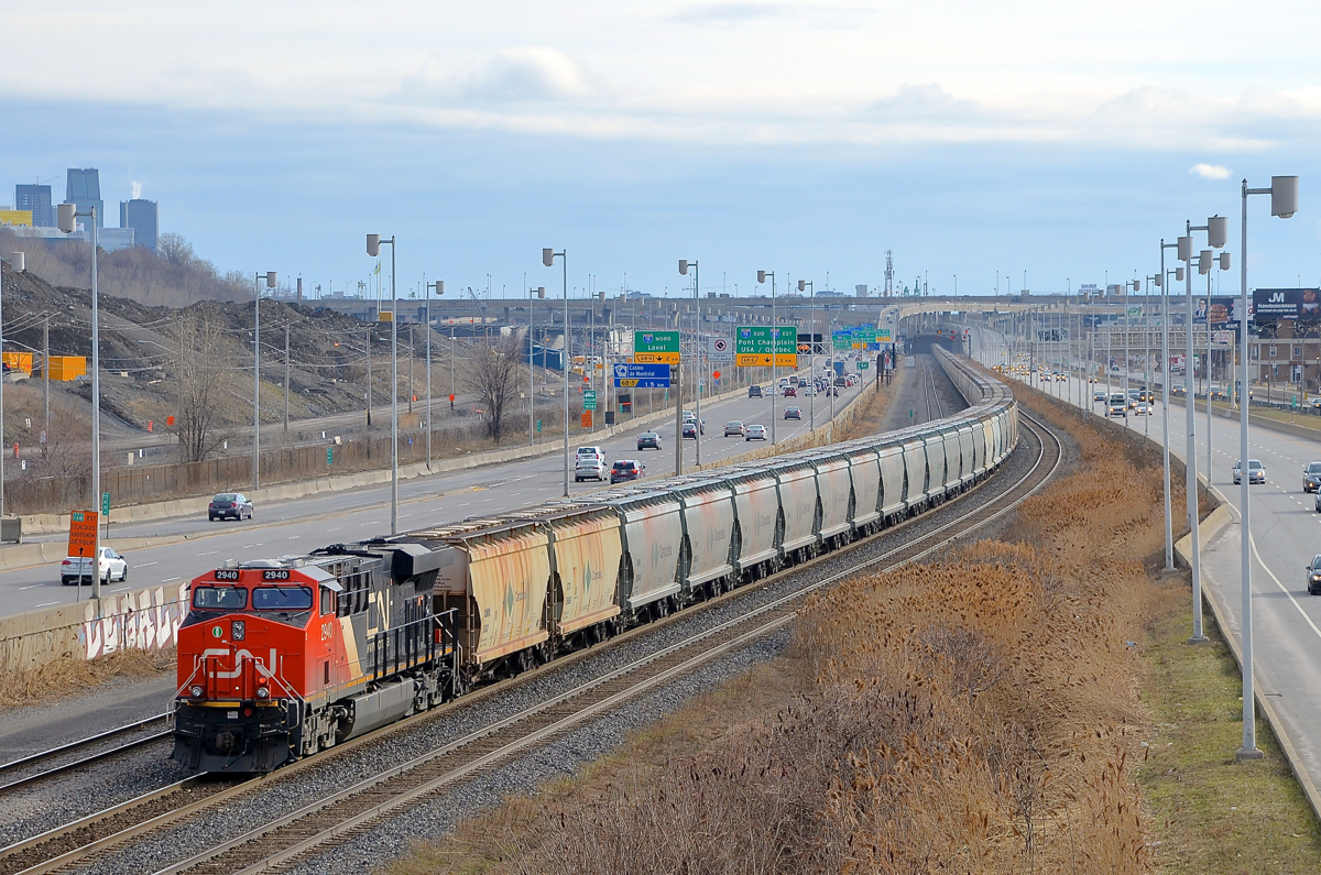 Marker light lit on the rear of a long potash train CN B730 with 152 loads of Potash destined for Saint John, NB is slowly starting to leave Turcot West in Montreal after changing crews. Power is a trio of ES44AC's, with CN 2934 & CN 2812 at the head end and CN 2940 bringing up the rear, with its marker light lit. At right is the skyline of downtown Montreal.