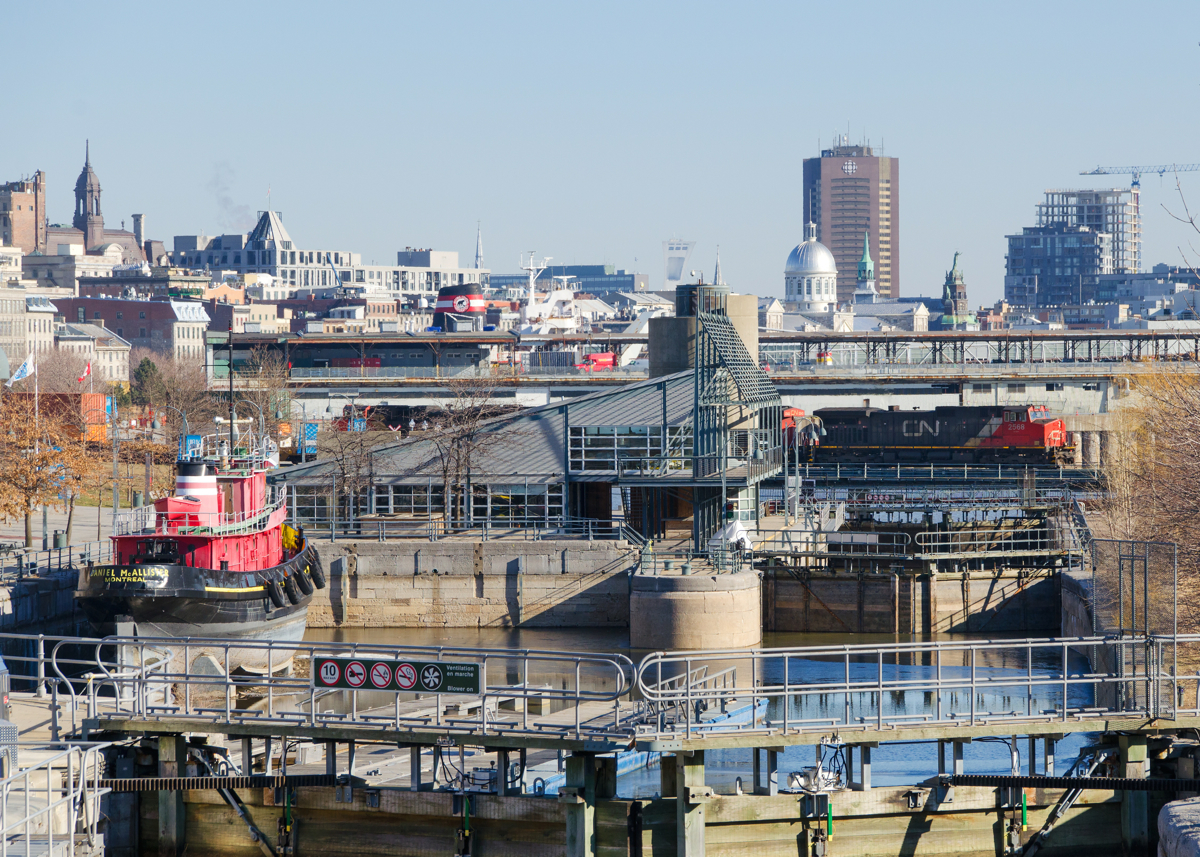Leaving the Port of Montreal. CN 2568 is leading CN 149 as it leaves the Port of Montreal. Visible in this photo are locks for the Lachine canal, a preserved tugboat, the stack of a laker laying over, the Olympic Stadium and Radio-Canada headquarters, among other things.