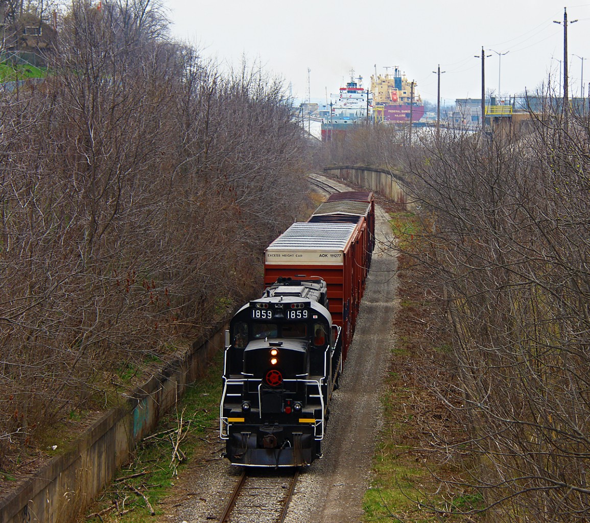 After working the Grantham Spur in St. Catharines, TR 1859 heads back towards Welland with four boxcars, including one hi-cube. From recent observations, it appears this is typically a Monday and Friday run. 1859 is without a doubt the cleanest unit Trillium has, and it appears the crews may take pride in cleaning it, something unheard of on class 1 railroads. The conductor clearly has some knowledge of railroad photography, as he very nicely dimmed the lights for me, and proudly waved. In the distance, two ships make their way through Locks 4-6 on the Welland Canal, while another descends Lock 7 just to the right of the photo.

Back when this was CN's mainline to and from Buffalo, it was double track. That changed around the 1970s, and only westbounds took this route downhill due to the ridiculously steep grade, as well as the odd local like 549. Bridge 10 was dismantled in 1997, effectively splitting the Thorold Sub in half and pushing all trains onto the Stamford Sub. Today it is the Thorold Spur as used by Trillium. Arnold Mooney's shot from just months prior to Bridge 10's dismantling shows some of the few changes that have occurred. 

http://www.railpictures.ca/?attachment_id=7959

As always, significant tree growth as occurred. And anything longer than a stubby local just doesn't happen anymore, besides when CP goes on strike. Emergency detours on CN do warrant a possibility, but taking the Hamilton Sub the entire way would offer much less hassle and would be safer. For now, enjoy Trillium!