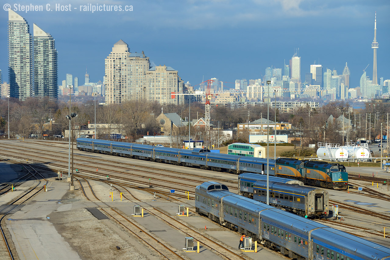 The Toronto skyline is lit up in the brilliant late winter sun and stainless steel of VIA's classic Canadian equipment reflects the blue skies above.
Vancouver-Toronto #2 arrived a few hours earlier, spent time at the fuelling racks, set off the dining and park cars before parking the remainder of the train in the yard as seen waiting for their turn for maintenance and cleaning. 
#1 is also preparing for an 8 PM departure, with the park car in the foreground and the rest of the train including a pair of locomotives behind me. #1 will reverse from TMC to Union Station to board passengers and depart for Vancouver. Other than the change of location and lack of CP F's on the point of this train, the look of this train is simply classic, ride or shoot it while you can folks!