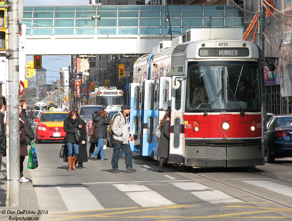 The 501 Queen route during rush hour can be a busy line (streetcar ridership on the Queen corridor is apparently higher than that on the Sheppard subway or Scarborough RT), thus its use of articulated ALRV streetcars over the conventional CLRV cars. TTC 4215 has just stopped at Bay Street as patrons step off the sidewalk to board, fumbling with their wallets and purses for tokens or exact change.

The UTDC-built ALRV fleet was supposed to be the first to go once the new Bombardier streetcars arrived, but due to Bombardier's ongoing supply chain issues and failure to be able to keep to any delivery timeline, the aging ALRV's have been granted a small reprieve, with a number of cars being overhauled to keep them going a little longer (and the bill will likely be going to Bombardier as contract failure penalties).