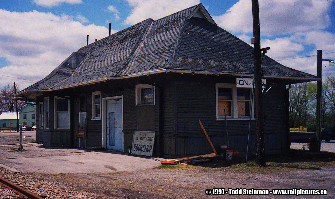 Last month and to my surprise, I found the Jarvis station on the move. When I was browsing through my collection, this photo brought me back to when I was a youngster. Typical CN fashion in the later years when they're stations needed maintenance...plain dull colours. Jarvis was painted in the dull grey, with blue and orange doors...plain and simple in design replacing the original wooden doors that seemed to be more fashionable in design. 

For those who have read my bio, it is this style that I still hold dearly to me...as plain as it is, it was still surprisingly appealing to me. 

Thankfully, the building was repainted when Michaud Fine Woodworking had owned the station. This design was more typically found on the CN's stations from the 50's...usually reversed with the red as the main colour on the building with cream trimmed windows. You can view the station at it's first stage of moving here: http://www.railpictures.ca/?attachment_id=23995#sthash.y2bCDtOD.dpuf 

Of note...the tracks and station aren't the only thing that have or will be disappearing...in the background, to the left, is the old railway hotel which burned down a short time after this photo was taken.