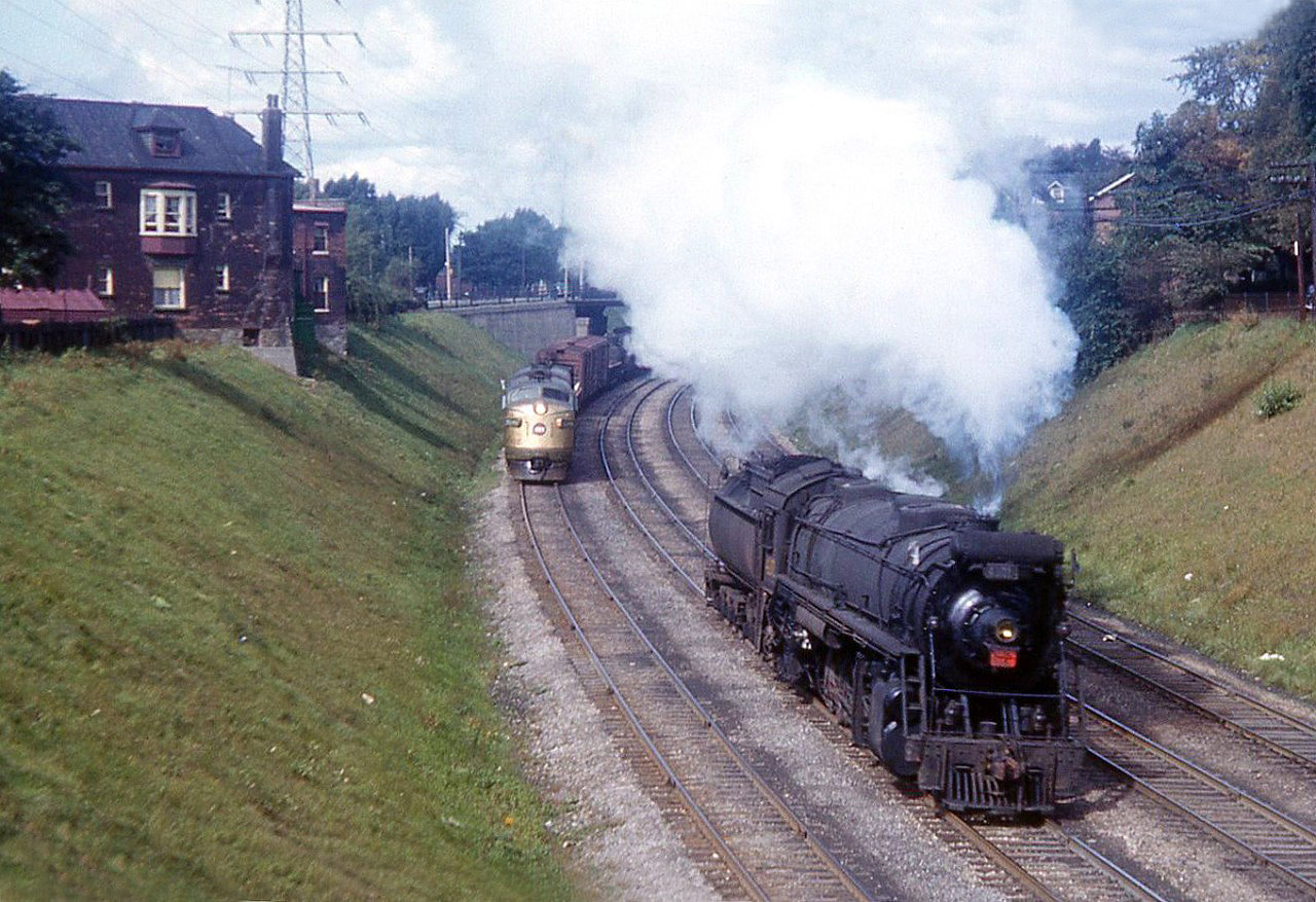 A Canadian National 4100-series 2-10-2 "Santa Fe" type steamer is returning to Spadina from Mimico, passing a nearly new golden-nosed GMD F-unit on an eastbound freight. This view is looking west on the CN Oakville Sub, just east of Jameson Avenue in the background. The houses on left, part of the South Parkdale neighbourhood, would be demolished for the Gardiner Expressway a few years later.