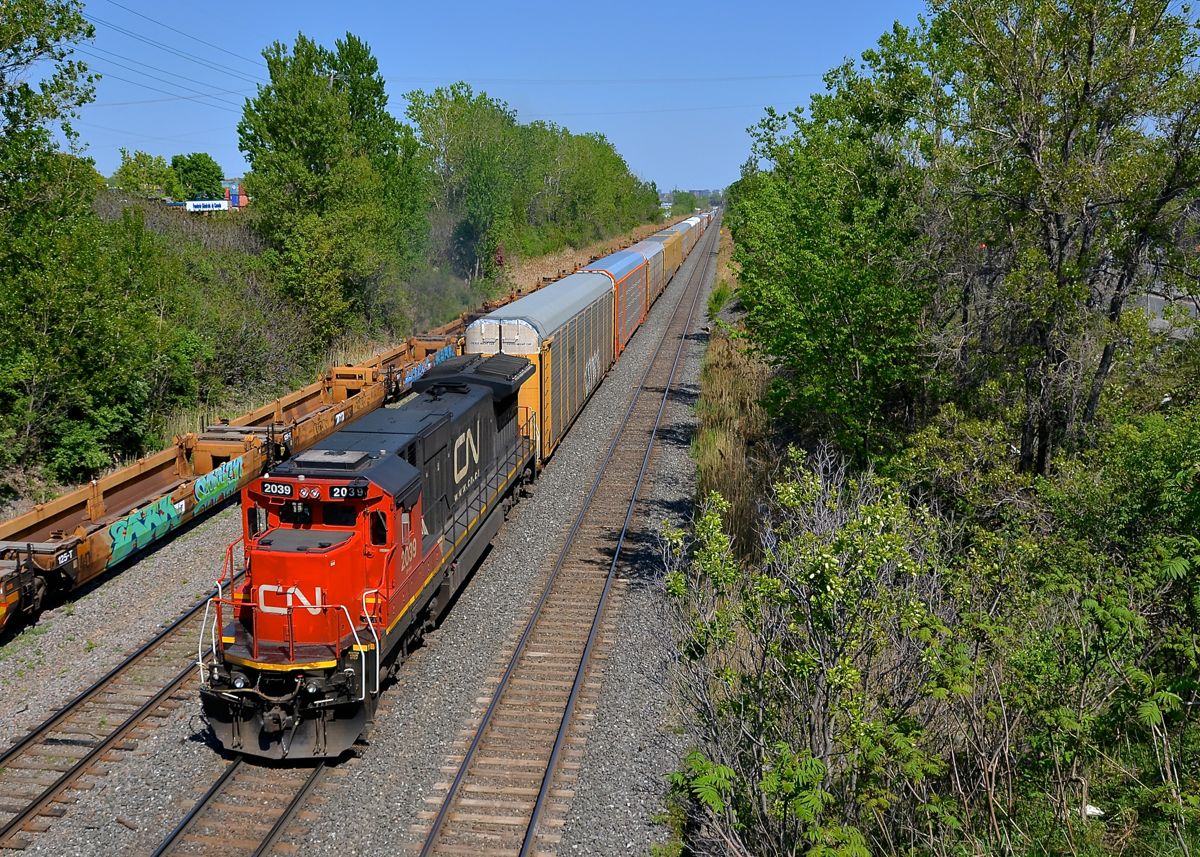 A solo C40-8 past stored well cars. A shorter than usual CN 401 is powered by just a single C40-8 (CN 2039) as it passes stored well cars on CN's Montreal sub near the entrance to Taschereau Yard.