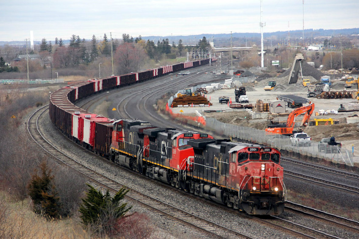 An east bound Herzog, cn ballast train rounds the curve at Whitby. Three different CN style logo,s on three units. 2501  a little faded but up front and looking good. If you look closely at the top of the cars you will see solar panels. These cars are operated by satellite threw GPS and release the exact amount of ballast where needed along the right of way. For those who enjoy this location a little safety note. The wild life seems to be returning and along with it a black coyote, which was spotted by the bridge April 30th. Believed to be of a mixed breed and showed no fear.