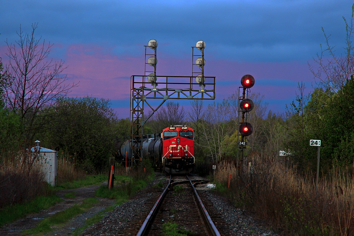 Early dawn begins to hit the nose of CN 2341 as it idles away just short of the Port Robinson West interlocking with CN 422. At the head end, 331's death bed lies in the consist (loaded Vinyl Chloride tankers). From past experiences at Port Robinson, including many very early morning trips go out of Port Robinson Yard and almost half way to Thorold Stone Road was quite common. I never bothered to stay out past 6am though as yard operations died until around 9am when Port Robinson became a barrage of granny drivers that like to drive 20 below the limit. I've even been screamed at multiple times to slow down in the downtown area while driving the speed limit (both were people standing almost in the middle of the road). As of very recently though, CN 422 has left Port Robinson shortly after 0600 on several occasions, where as before a 0900 departure was the earliest you'd see. This new scheduled time or whatever it may be is good for me as I don't have to deal with the slow knuckleheads in the area who frequently tap their brakes for invisible cars, or the crazy locals standing in the middle of the road screaming at me. However, another advantage appears to be the lighting, which was quite mellow yet not the drabby overcast kind of mellow. The sky made short work of that as it was completely overcast only a few minutes later. 

422 would throttle up about a half hour after I left. As it had consistently been so recently, 422 was about 11000 feet, however dozens of 89 foot autoracks, 89 foot flat cars and 86 autoparts cars meant only 140 cars were needed to make up that length.

As for this particular interlocking, like many others on the Stamford Sub, it is a wye which leads to other subdivisions. The track to the right goes to the CN Thorold Spur. This wye is mostly utilized at night it seems. Oh, and the Geep yard power that used to be at Port Rob, I haven't seen them in months. All the six axle units have been doing all the switch grinding work it seems. The rails in the foreground show relatively clear signs of what appears to be wheel slip. Well, considering this is a takeoff point for 150 car behemoths, I guess that's not a surprise.