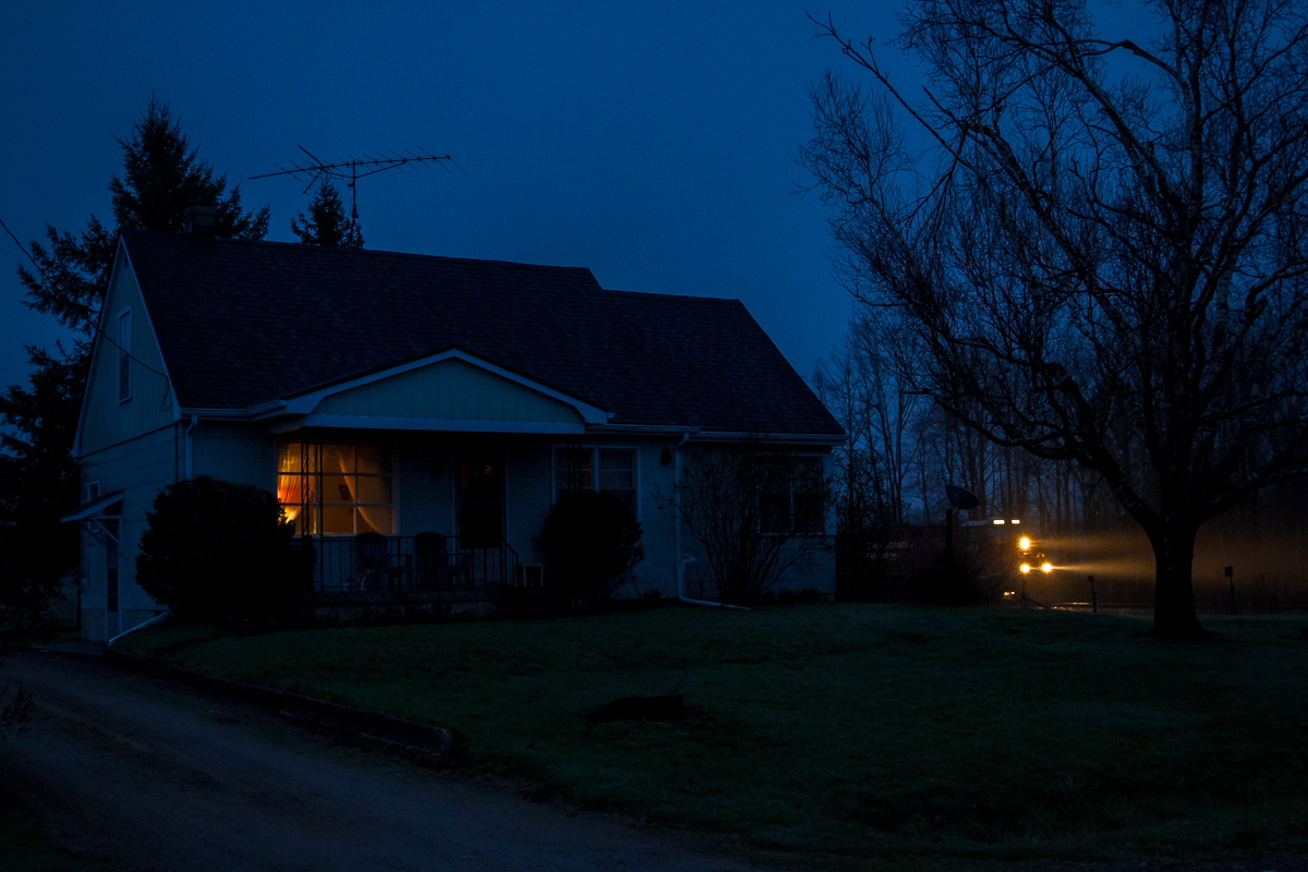 Twenty minutes after sunset, Canadian Pacific's Chicago to Montreal stack train no. 142 is seen passing by a farm house on a gloomy spring evening in Flamborough, Ontario. 

Having biked to this location from my house (about a quarter mile down the road) I managed to beat the train with less than a minute to spare. This didn't leave me with enough time to set up a tripod but with a frenetic guess at my exposure and steady hands I was able to save the shot.