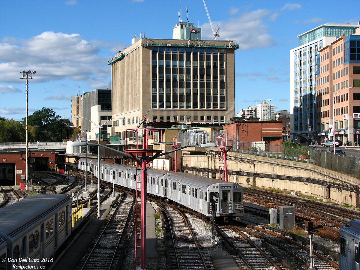 A train of Bombardier T1 subway cars depart the Toronto Transit Commission's Davisville Yard, pulling into the third platform track at Davisville station in order to enter service southbound on the Yonge subway line for the evening rush. Towering in the background (although small by today's hi-rise standards) is the W.C. McBrien building, the organization's current headquarters that was built over Davisville station circa 1958. On the left is the shop building where trains are locally serviced, and on the lower left is a pair of old Hawker Siddley H1 cars, now relegated to work service and coupled to a work flat. All this is viewed from the old CN/Grand Trunk "Belt Line Branch" bridge the original "Red Rocket" subway cars were delivered on in the 1950's, which is now part of a walking trail.