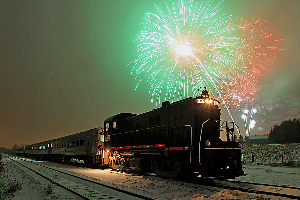 On New Years Eve 2009/2010 Judy and I were tasked by Rita and John Carroll, owners of the late Guelph Junction Express dinner and excursion train, with photographing their New Years Eve Special. The train came in from Guelph and was parked in the siding at Arkell while passengers feasted on a first-class meal. Just before midnight passengers debarked and stood in the snow for the countdown. At the stroke of midnight the sound of champagne corks being popped was joined by explosions of fireworks set off from a farmyard on the hill on the far side of the tracks. With our cameras firmly mounted on heavy tripods we took a series of long exposures as I ran around behind the line of sight with my Starblitz flash set at 1/16 power just to fill in some detail on the dark side of the locomotive. I had never photographed fireworks in a snowstorm before and I was impressed with how the dense, fine snow spread the colors all over the scene. It was a truly magical experience and one I won't soon forget!