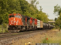 <b> HOT, HAZY, HUMID...</b> and with the hammer down! As it passes me at the old station site, CN 5657 (and two other units) leads this mostly tank car revenue freight up the Niagara Escarpment accelerating as it continues to all points west.