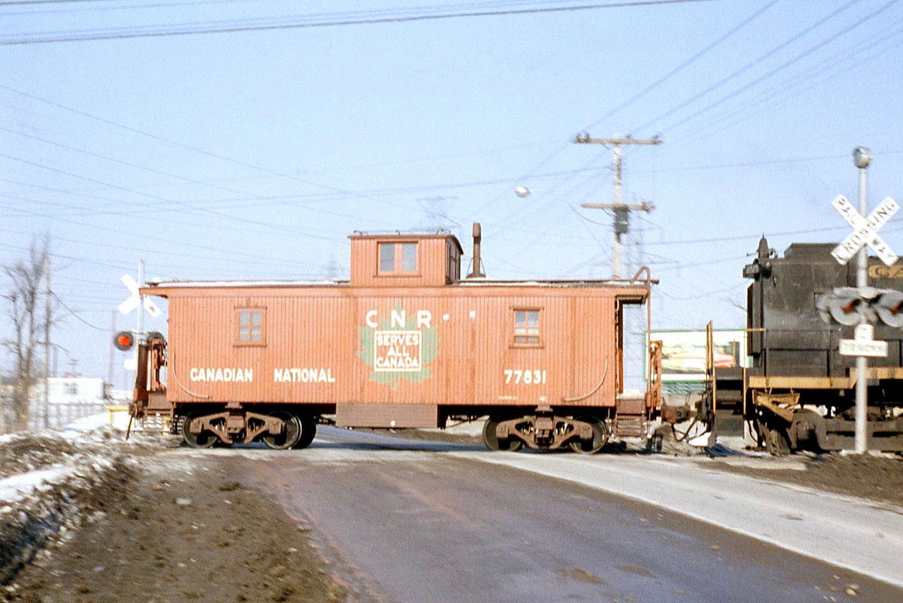 Canadian National wooden centre cupola caboose 77831 (not matching the typical CN offset-cupola appearance, as it was one of the few GTW cabeese transferred to CN) trails a CN S13 switcher across Kipling Avenue crossing in Rexdale, on the Brampton (soon to be Weston) Subdivision in 1963.

This crossing has since been grade separated in 1968, and just a stone's throw away is the site of the present-day Etobicoke North GO station. While Metrolinx currently owns the Weston Sub, CN locals continue to service the remaining industries (albeit, without a caboose).
