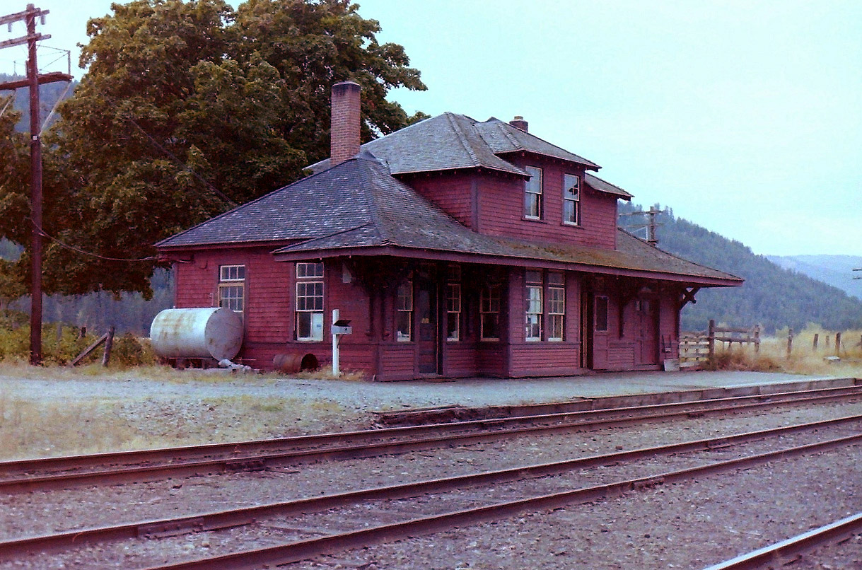 I was driving back to Vancouver BC on highway 3 when I spotted some CP buildings on the north side of the road at Midway BC. I pulled over, & walked around yards for a few minutes & there was no railway activity  at all. No rolling stock, just a soft wind. I took what pictures I could until I ran out of film. While there I took two pictures of the station. The attached picture turned the best. The other one taught me not to keep the camera strap too close to the lens. The hills in the background are in the USA. I'm glad the town kept the station, & used it to promote the local history.