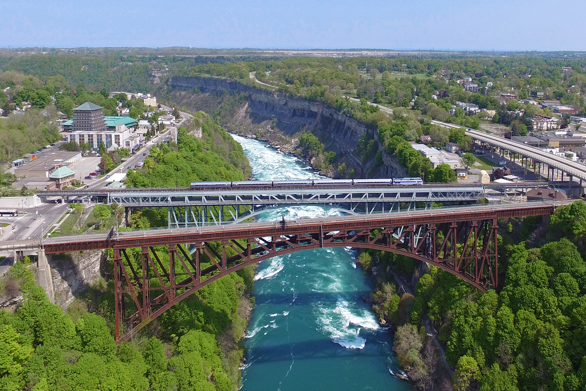 From my understanding, Arnold has the only photos on this site taken in the U.S, and could be contested as 'Canadian' pictures. Both of which included these two bridges, the Michigan Central bridge, and the Whirlpool Rapids bridge behind it. Nonetheless, here's my own borderline shot. Here, Amtrak 64 crosses the Whirlpool Rapids bridge with Phase IV Heritage 184 leading the way. The train has just departed Niagara Falls, Ontario station, and will soon be at the New York stop, or the ghetto version of what the Canadian side has. Sorry Americans... Much has changed since Arnold's shots were taken, as the Michigan Central bridge has been train free for nearly 15 years, when Niagara Falls paid CP $39 million to get out of town. Run through operations were diverted over CN to Fort Erie, which in all honestly is a much more efficient route to Buffalo, and likely helped persuade CP. CN also lost interest in the Whirlpool Rapids bridge with the Whirlpool Rapids bridge already a decent connection point from Fort Erie to Buffalo. Just prior to the Michigan Central bridge closing, freight loads were banned over the Whirlpool Rapids bridge. Since then, it is to my understanding only a few freights have crossed this bridge, the most recent in 2012 when a juvenile released the handbrake on a boxcar in the American Niagara Falls, and it rolled right over the bridge. I'm guessing CSX hauled it back? Nonetheless, it had been CN's intention to abandon their rights over the bridge for years. Unlike the other sad tales in the area, and many other railway bridges, CN did not own the bridge itself, but simply the top deck, as the lower deck has automobile traffic. Therefore, Amtrak assumed responsibility for maintenance of the upper deck a few years back, and it still goes today. With hope for significantly improved intercity passenger rail service in the next 20-30 years, perhaps this bridge will be used to it's full potential again. Oh, and the Whirlpool Rapids bridge is 28 years older than the Michigan Central bridge. Looks can be deceiving...