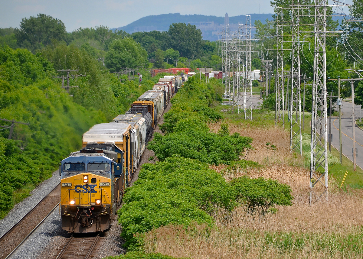 Mount-Royal in the distance. CN 327 is westbound through Pointe-Claire led by big GE product CSXT 631, an AC6000CW. In North America only CSXT and Union Pacific bought these units, and in limited numbers. Trailing is an ex-Seaboard SD50 (CSXT 8613). In the distance is Mount-Royal.
