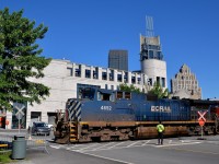 <b>BC Rail leader over a flagged crossing.</b> BCOL 4652 slowly leads CN 149 over a crossing which is being flagged on either side by a Port of Montreal employee on a sunny morning.