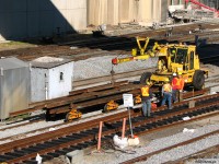 Lazy afternoon going-ons down at the station: a gang of Toronto Terminals Railway (TTR) employess work on new a track panel for replacing a section of trackage around Union Station, while their Swingmaster Swingloader passes by towing a load of old rail on bogies. Old wooden signal bungalows and modern galvanized steel ones mingle freely nearby, and new ballast is spread on neighbouring tracks that have recently been attended to. In the upper right, work continues on the Simcoe Street underpass project that will open to traffic in the future (you can see the remains of the old MofW storage building at the end of the Skywalk that was demolished).