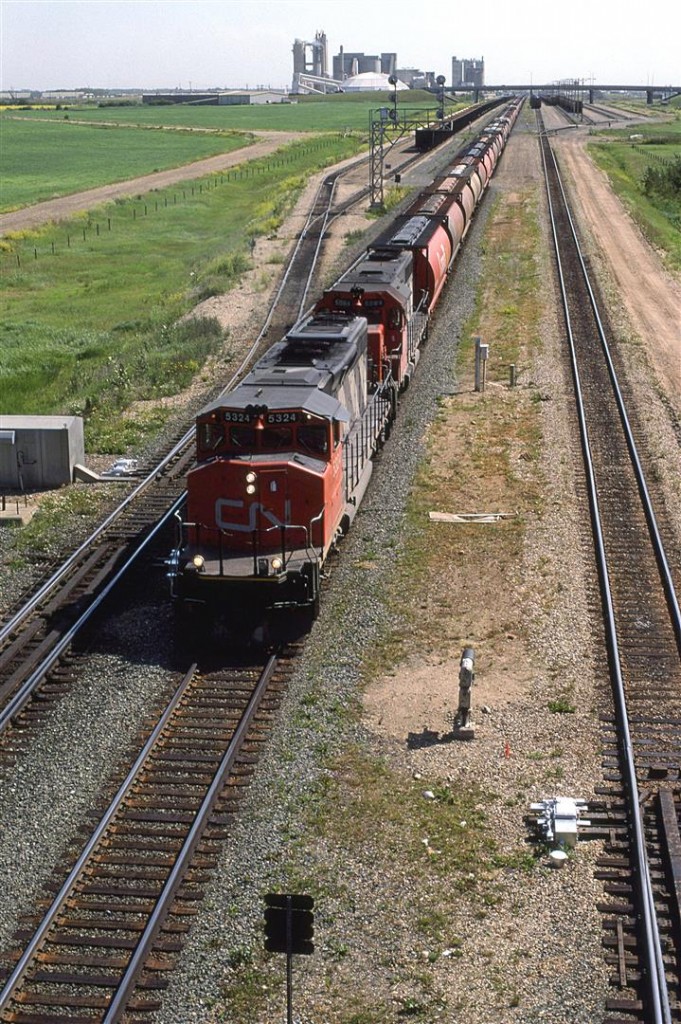 A loaded grain train heads out of Edmonton, headed for the west coast. In the yard to the left of the train can be seen a set of empty Sulphur cars. They are either going to leave by heading NW on the Sangudo Sub or South on the Camrose Sub (Ultimately, using the Brazeau Sub) to the sour gas fields in the foothills of the Rocky Mountains.