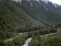 This view is almost obscured too, however, there are likely ways that it couyld be had from a slightly higher vantage point.
The eastbound manifest is through Illecillewaet siding, but still has several more Kilometers to go before the engineer can slack off on the power at the crest of Rogers Pass.