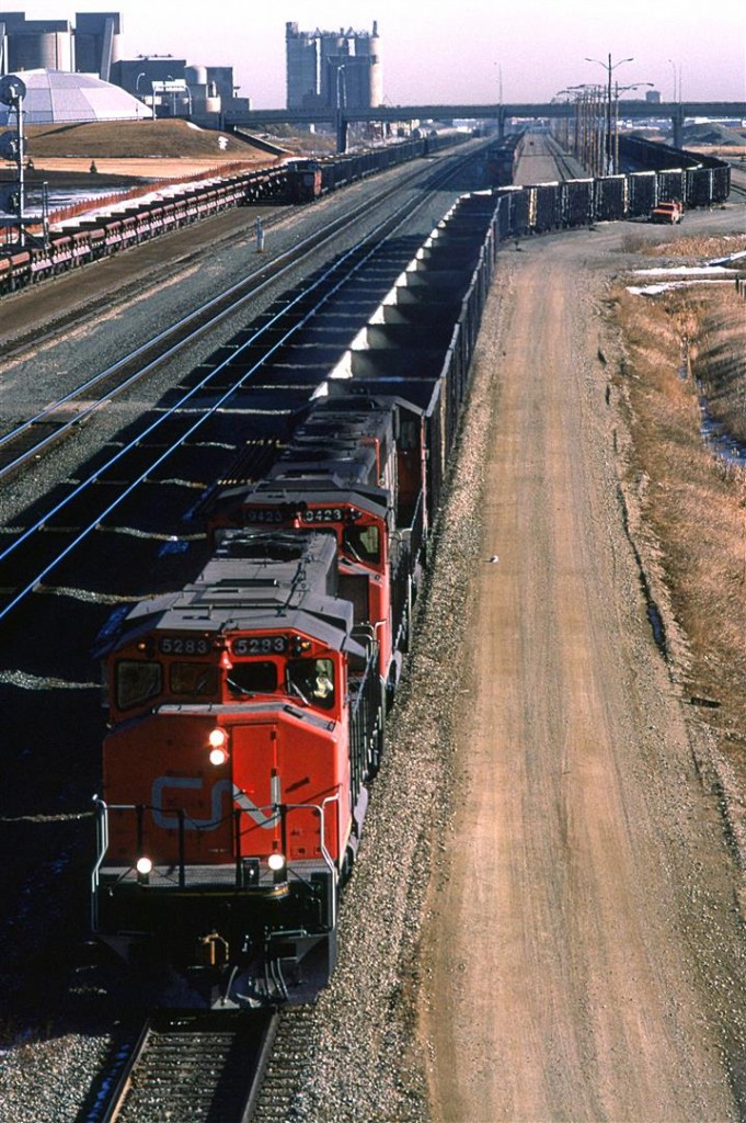 An empty coal train departs Edmonton for the coal fields around Hinton, Alberta.
Also in the yard is a loaded sulphur train with a caboose on the west end. That likely means that it arrived from the Kaybob via the Sangudo Sub. Union Junction, just beyond the head end of that string of cars, is where the Sangudo Sub joins the Edson Sub mainline. Due to the configuration of that junction, the train entered the Edson Sub and had to back into Bissell yard.
There is a soon-to-be eastbound grain train and a string of ballast cars in the yard, too.