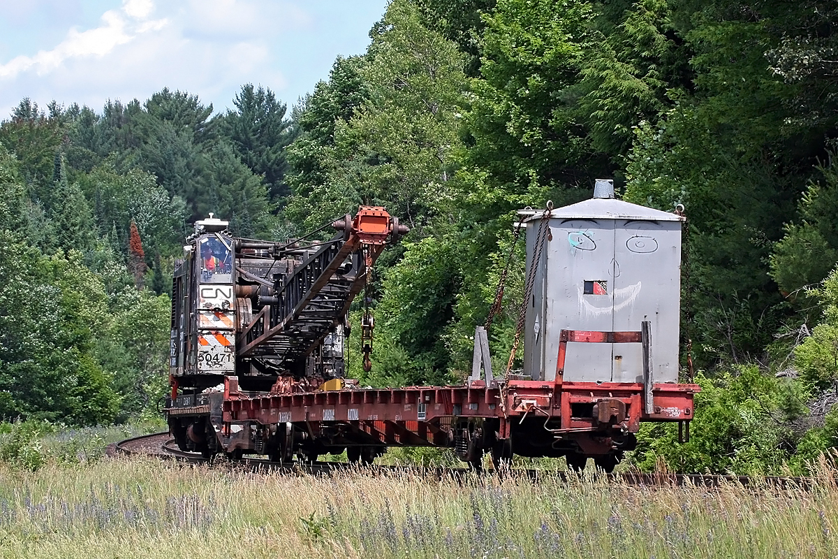 Out of the woods the Tin Woodsman cometh! 

Sorry - but what with the painted face and upended pail on the roof vent of the little repurposed signal shack on the crane's flat car, I couldn't help but think of the character from the Wizard of Oz! 

Hearing something like a coffee truck or dump truck air horn sounding a Rule 14(L) at the South Lancelot Road crossing, I whipped on down to Mile 138 to see this Ohio rail crane preceded by a Hi-Rail truck. Having only my 100-400mm lens with me (I'd been loading the car up with empties for the beer store and didn't expect to see a train, rather I was kinda hoping to get a shot of the cougar of the quadruped, NOT biped variety, that's been hanging around my property there lately) I couldn't get far enough back to get a shot of it out in the open. I fired off one shot of it partially obstructed there then headed down to the big curve at Utterson (Mile 146) to get this shot as I knew that section of track would be clear of foreground clutter.