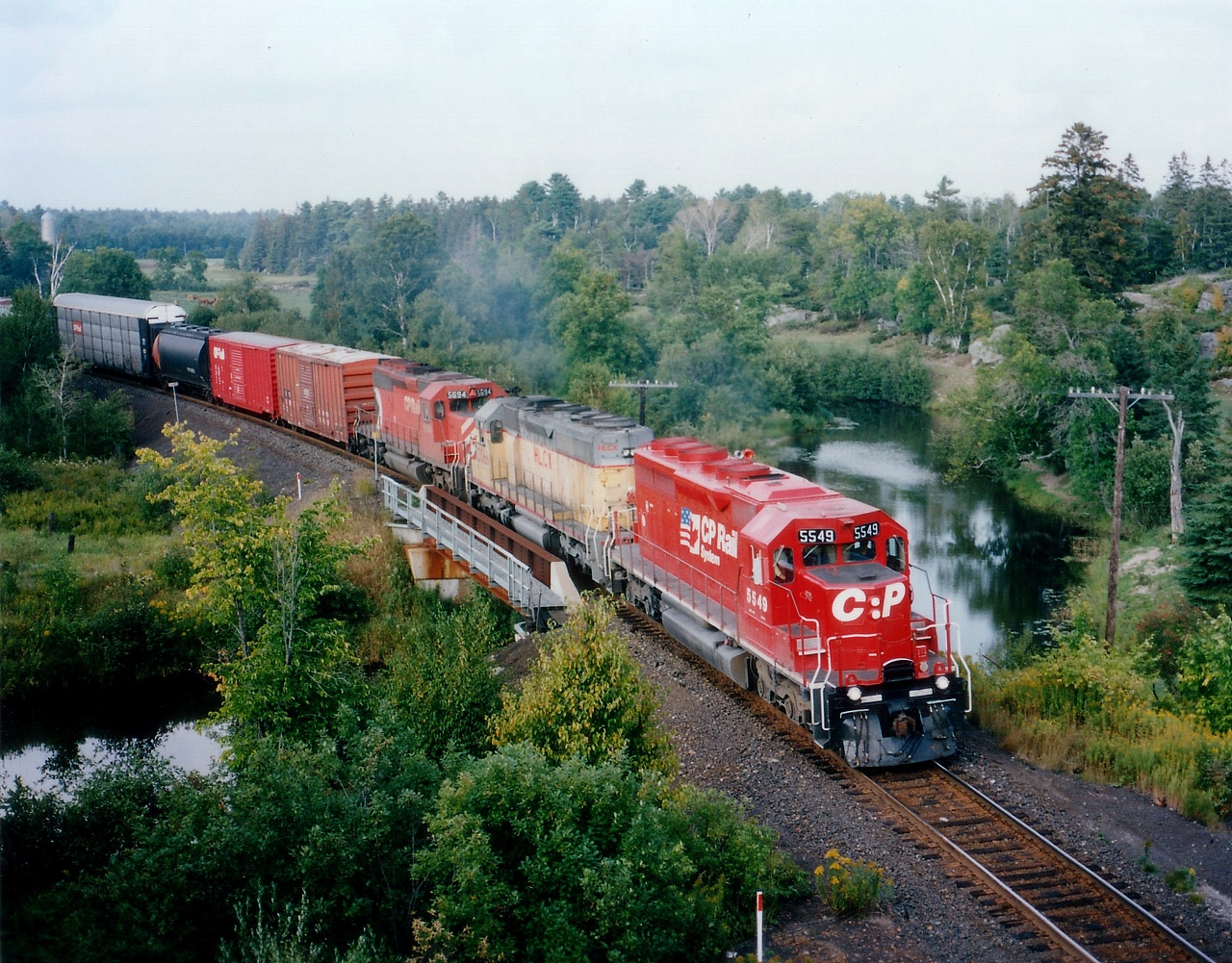 CP 5549, HLCX 3066 and CP 5694 make up the power on this days' Winnipeg-Toronto train #474 as it is about to duck under Hwy 69 on its way into Britt. The HLCX was a former UP, same number. The Still River looks rather peaceful in this photo. Dry summer, I guess.