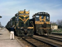 The Canadian National station operator at Glencoe stands on the platform with his train order hoop, about to pass orders to a westbound freight behind GP9 4588 in May 1968. SW1200RS 1212 waits on the passing track at the station, its crew giving a friendly wave out the cab window.