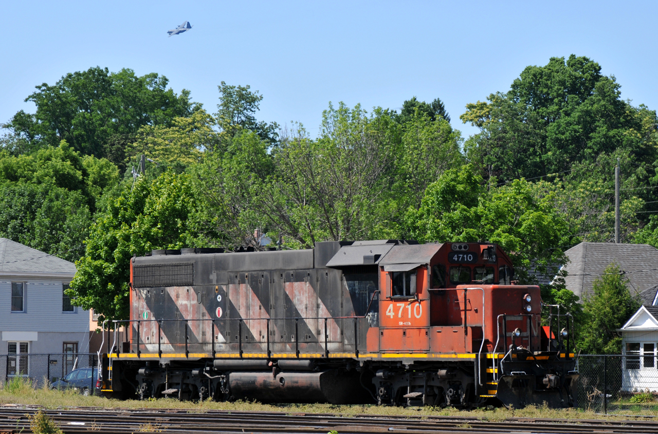 CN 4710 spends the weekend shut down in the locomotive track at Brantford, as a Canadian Forces C-130 circles overhead on approach to the airport