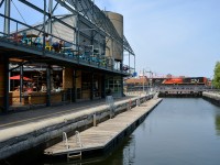 <b>Over the lock and past the market.</b> After coming into the Port of Montreal light, GP9's CN 7256 & CN 7075 head back with a short train. They are crossing over the eastern end of the Lachine Canal, where a lock exists for pleasure boats and passing the Éclusiers market at left.