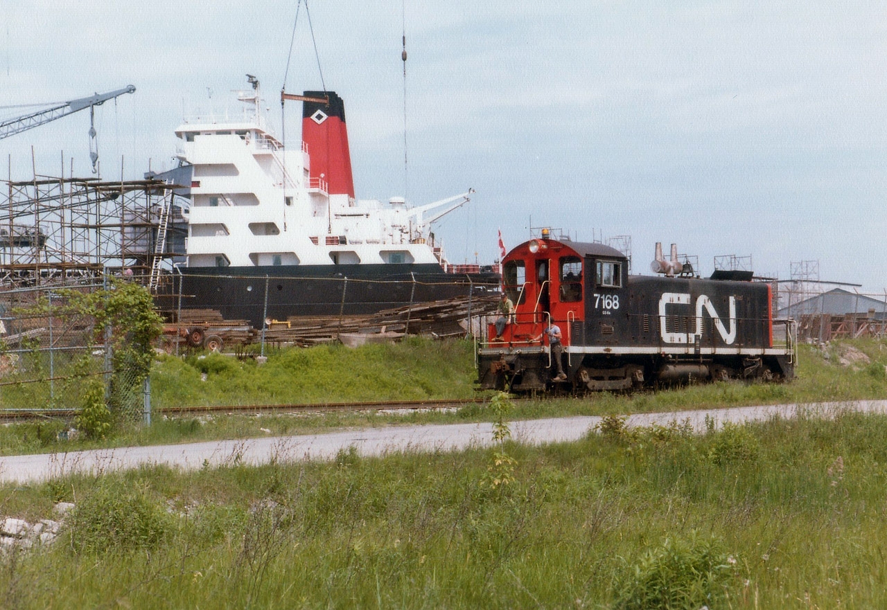 CN 7168, the resident switcher out of Merritton back at this time, runs back in the Port Weller Drydocks to fetch a couple of freight cars. The unit is just about to enter the fenced off area seen at the left of the photo. Ship under repair in background not identified other than it is part of the Algoma fleet. After CN gave up the industrial trackage in St. Catharines to Port Colborne Harbour (Trillium) in the late 1990s/early 2000s, the spur line north of the QEW was removed in stages, and now only runs as far as Bunting Rd and Eastchester, stopping just short of going under the QEW's Garden City Skyway. CN 7168 was one of the SW8s on the roster, of which all were retired by 1989.