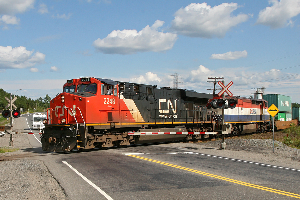 Heading north on the CN Bala Sub a stack train crosses the Trans Canada Highway with an enthusiastic wave from the conductor.