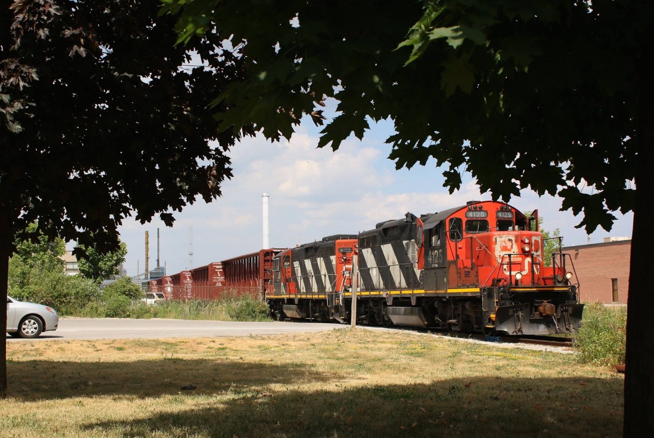 The temperature with the humidity is sitting around 38 degrees. There is little the crew of train 551 can do but open every possible door and window on their veteran GP9RM just to catch whatever breeze maybe outside the cab. I've taken to the shade of the few trees nearby as the crew switches out the lumber yard on the old Townline spur, which is all that remains of the original North & Northwestern Railroad line through town. The line was rebuilt with a grade separation through Milton in 1960 when CN's Toronto's Mac Millian yard opened north of the city.