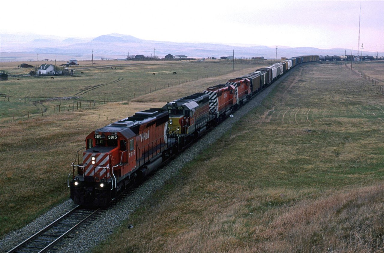 I just graduated, and we were on a road trip that would take us to the west coast, all the way to California, and then back up through the national Parks of Arizona, Utah and Wyoming.
We caught this westbound manifest west of Cowley. Note the leased Algoma Central SD-40.