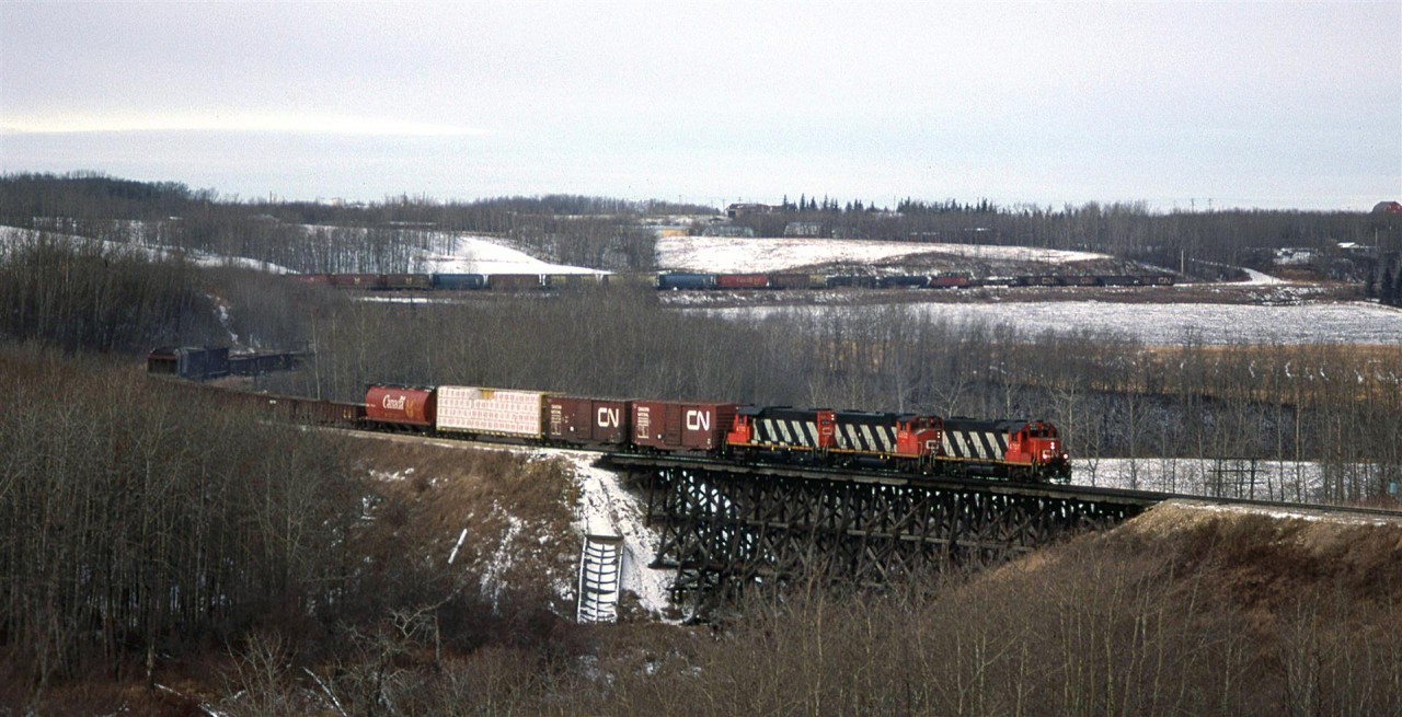 This is the Westlock Sub, just north of Edmonton, where it crosses the Sturgeon River. The train is the daily (or near daily) southbound manifest from McLennan.
This train is hauling wood products on the front, and on the rear we see grain and chemical/petroleum cars. But what is most interesting are the gondola and ore cars. I seem to recall that these would come from Hay River NWT and they are a metal concentrate. It would be shipped to Calgary, and ultimately to the smelter at Trail BC. I seem to recall seeing this material on train #484 from Edmonton to Calgary.
Note the caboose passing some ballast cars. That siding is no longer there.
....and what is that ribbed thing on the bank of the trestle abutment?