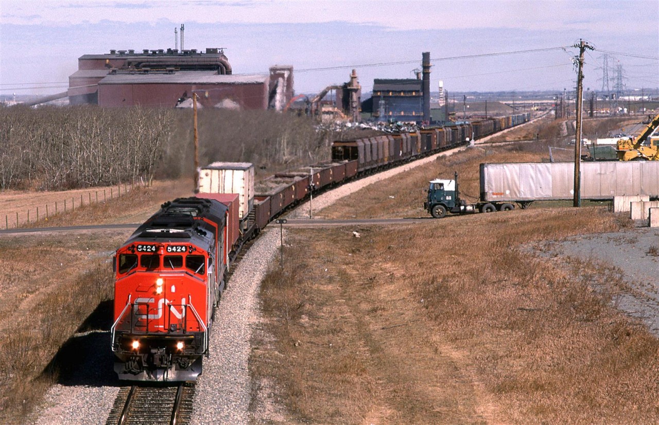 Here, we have the daily train from Edmonton to Calgary on the Camrose Sub in eastern Edmonton.
This train has the usual few TOFC/COFC up front. Next there are several dozen cars of ore concentrate that came in from Hay River, I believe, that is destined to be smelted at Trail BC. After that is the regular freight - mostly in box cars (wood products?).
The Stelco steel plant is prominent in the background and truck fanatics might find the vehicle on the right interesting.